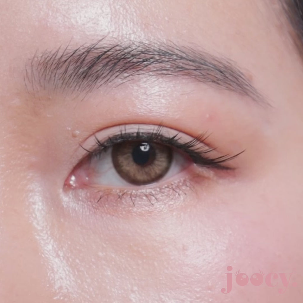 A macro close-up video of a single eye blinking on a fair-skinned model to show the joocy light honey brown lens in shade Exclusive. The luminous honey-gold sunburst gradient delivers a glamorous tiger-eye dimension on deep skin tones too.